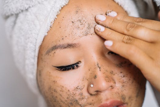 Woman with a head towel applying facial scrub for skincare routine.