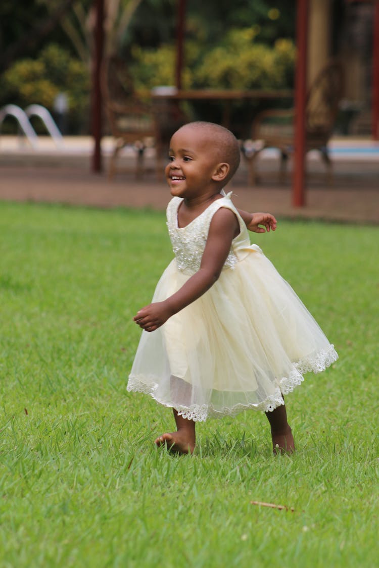 Little Girl Wearing White Dress Walking On Green Grass 