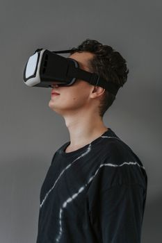Side view of a young man wearing a VR headset, immersed in virtual reality against a gray background.