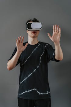 A young adult wearing VR glasses explores immersive experiences with hands raised against a gray background.