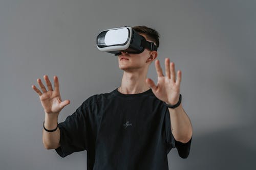 A Man in Black Shirt Standing Near Gray Wall while Wearing VR Headset