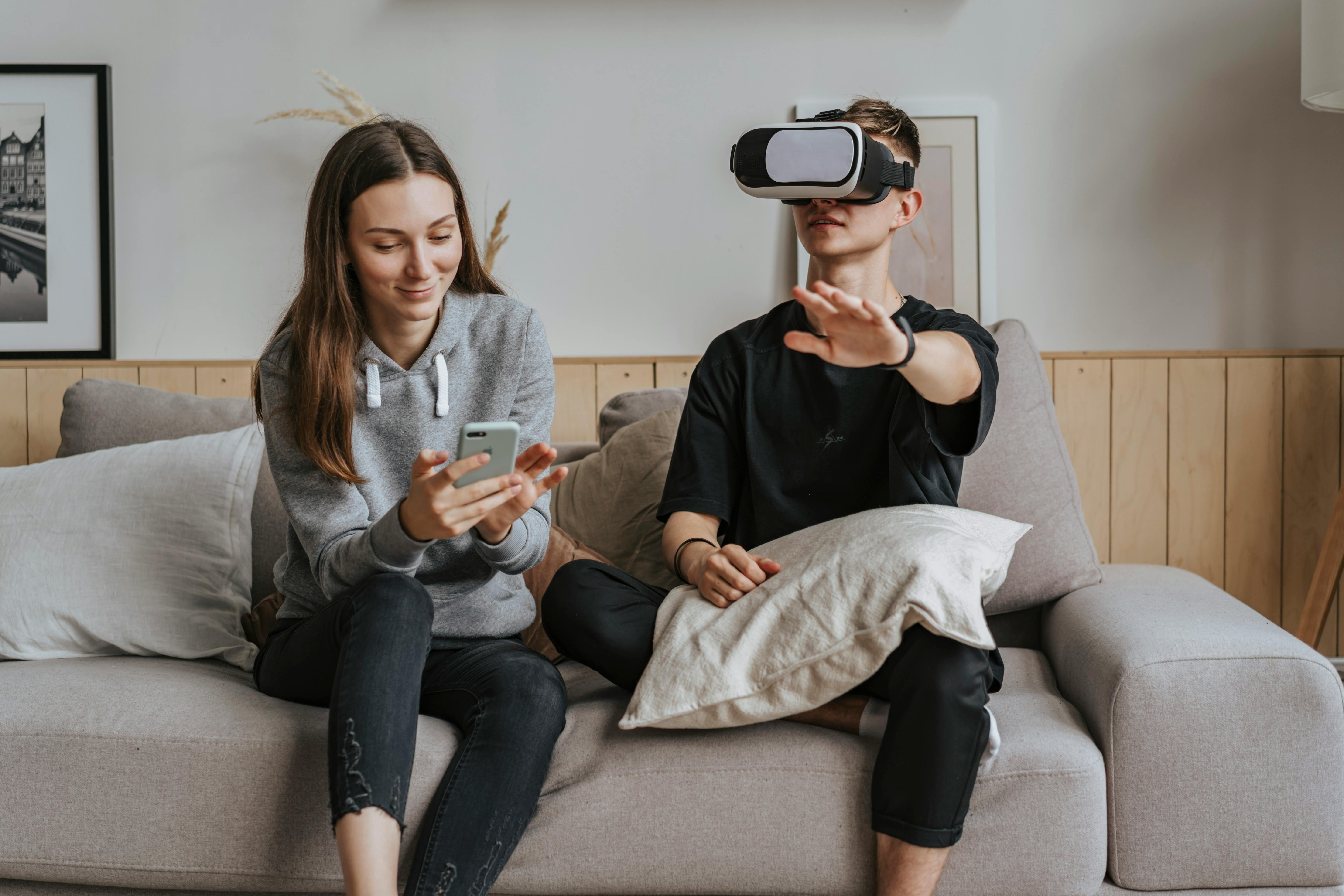 a woman busy using her cellphone while sitting beside a man wearing vr headset