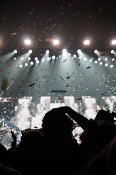 Silhouetted crowd enjoying a concert with vibrant confetti and bright stage lights.