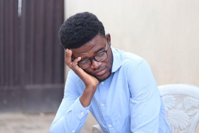 A man in a blue shirt resting his chin on his hand, deep in thought