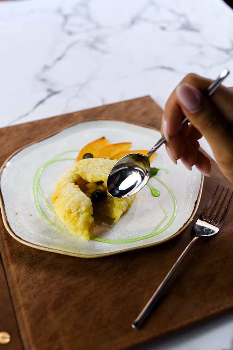 Person Holding A Spoon Near A Plate Of Food