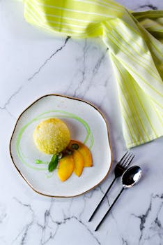 一份风格精美的甜点，盛在陶瓷盘里，盘上点缀着杏片，摆放在铺有餐具的大理石桌上