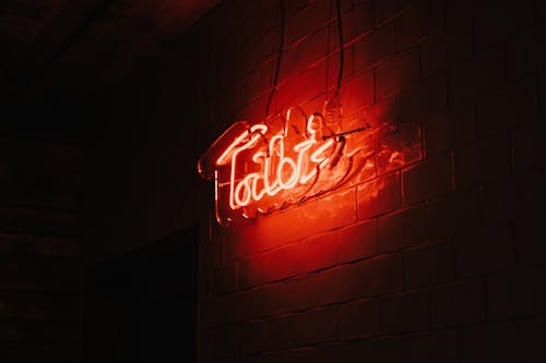 Low angle of shiny neon title on signboard on building brick wall in darkness