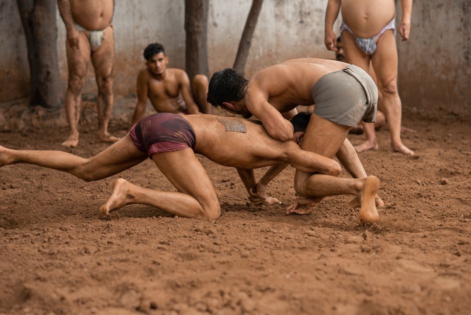 Two men engage in traditional Indian wrestling in a mud arena, showcasing skill and culture.