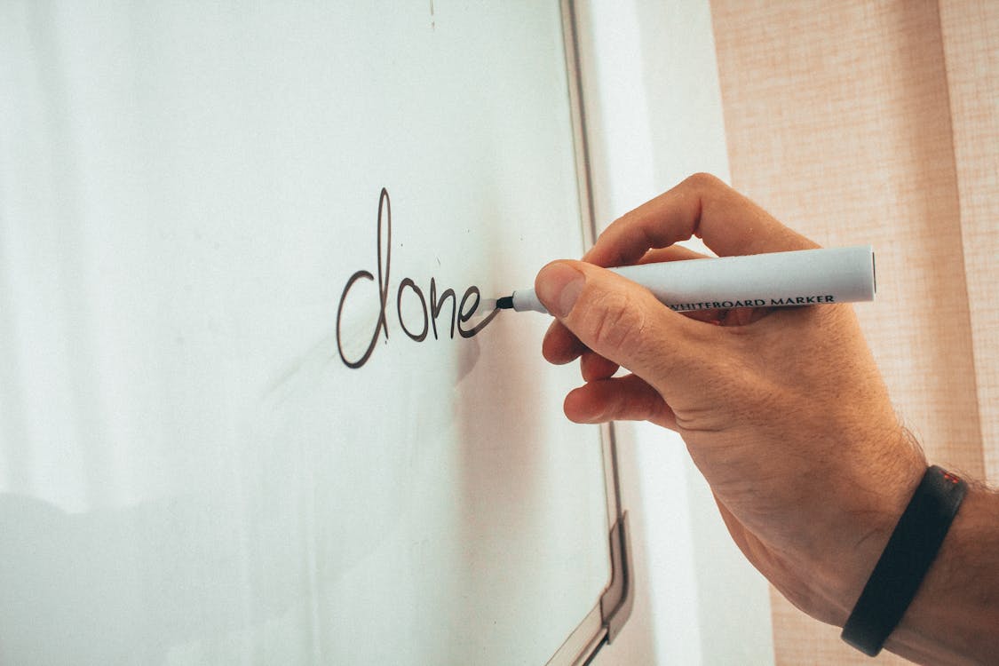 Free Crop unrecognizable male coach writing done word on whiteboard during presentation in light office Stock Photo