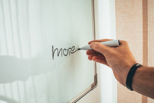 Crop unrecognizable man writing more word with marker on whiteboard during creating new startup in light workplace