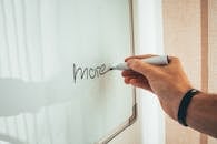 Crop unrecognizable man writing more word with marker on whiteboard during creating new startup in light workplace