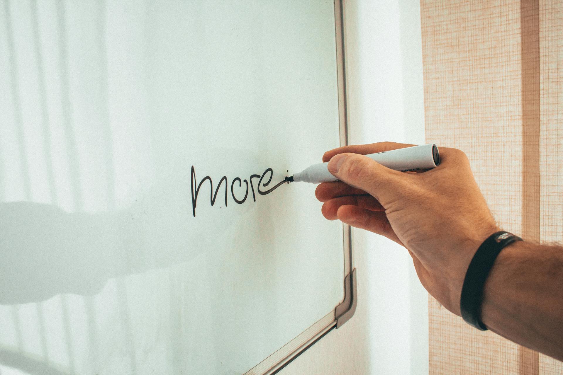 Crop unrecognizable man writing more word with marker on whiteboard during creating new startup in light workplace