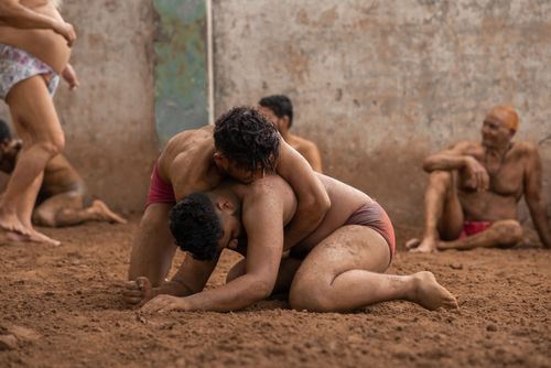 Free Men engaging in traditional wrestling on a mud arena, demonstrating cultural sports heritage. Stock Photo