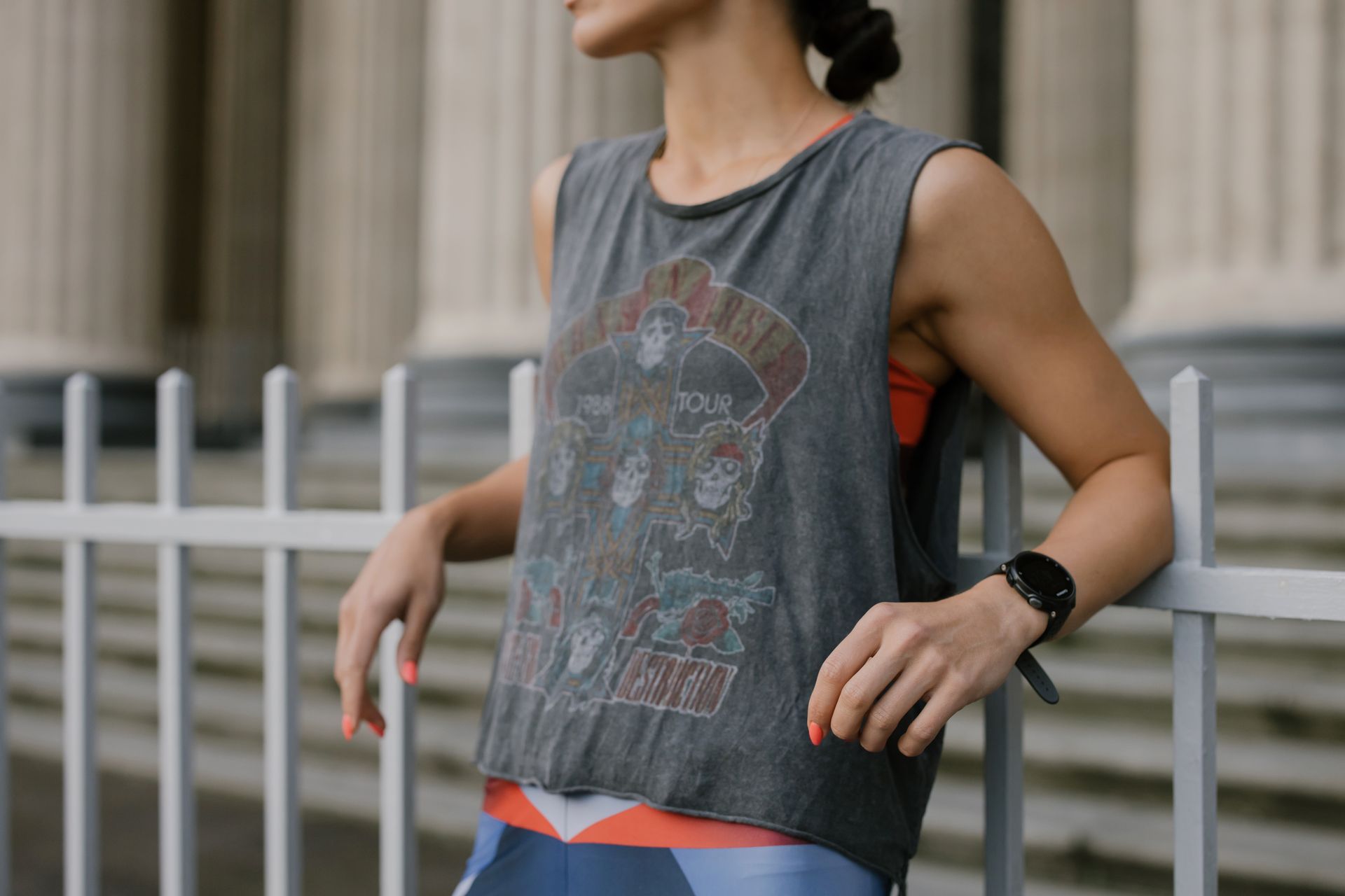 A fashionable woman in a graphic tank top leans on a city railing, blending fitness with urban style.
