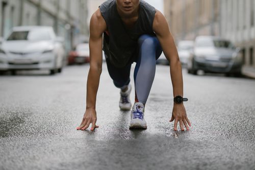 Free Determined woman in athletic pose ready to sprint on a wet city street. Stock Photo