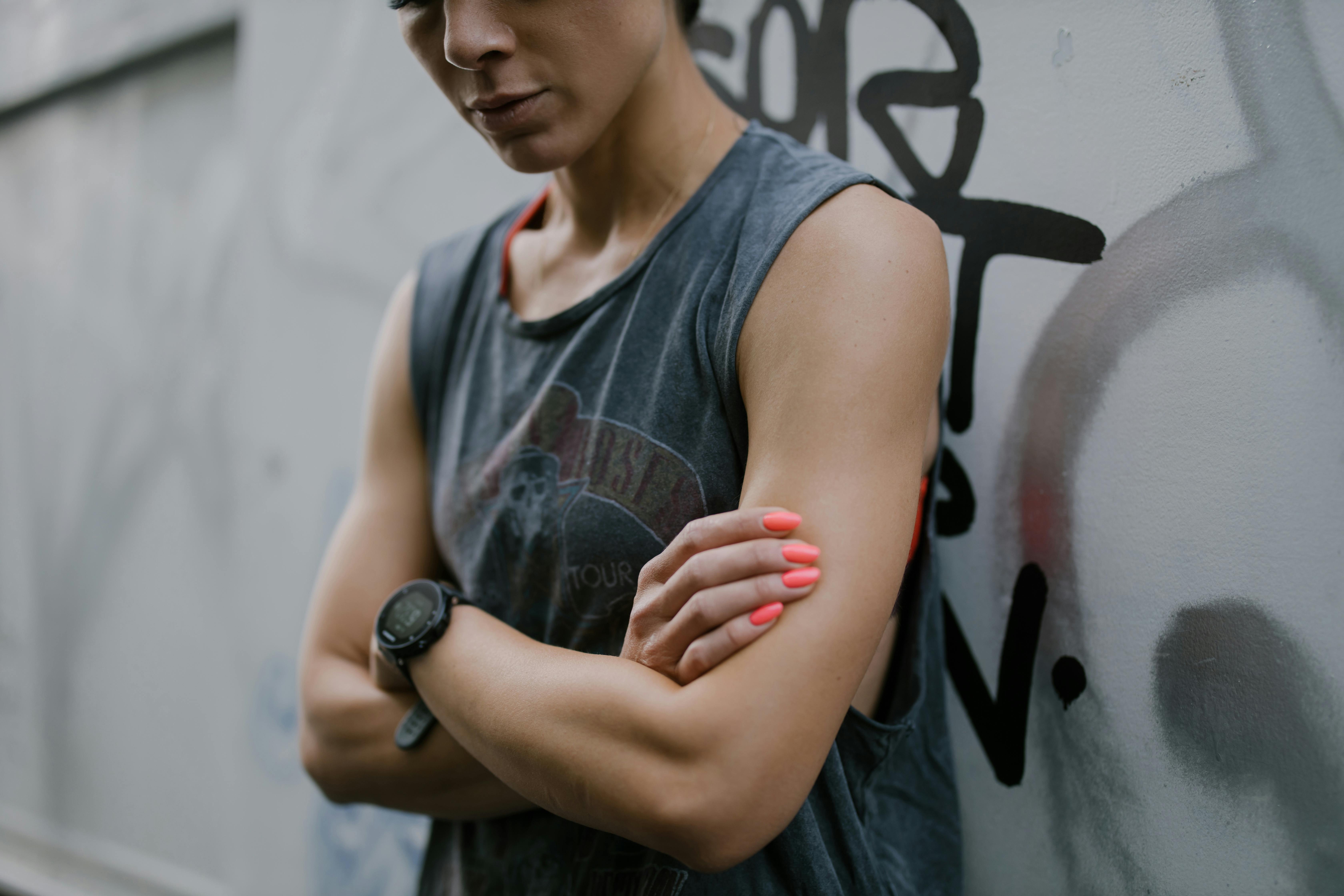 Close-up of a woman in a gray tank top standing against a graffiti wall with neon nails.