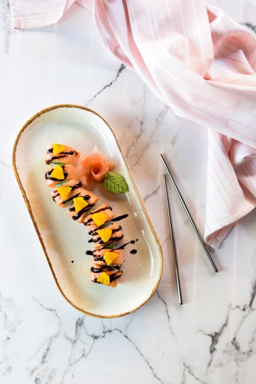 Free A visually appealing sushi roll plated on a marble background with elegant chopsticks and a pink napkin. Stock Photo