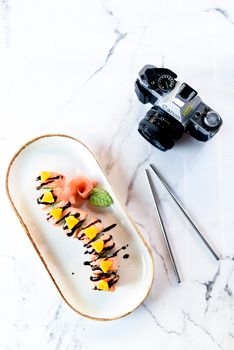 Delicious sushi rolls arranged on a marble surface beside a vintage DSLR camera, highlighting modern and traditional aesthetics.