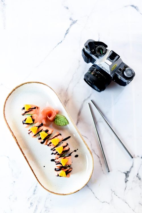 Free Delicious sushi rolls arranged on a marble surface beside a vintage DSLR camera, highlighting modern and traditional aesthetics. Stock Photo