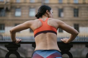 Woman in an orange athletic top showing defined back and shoulder muscles outdoors