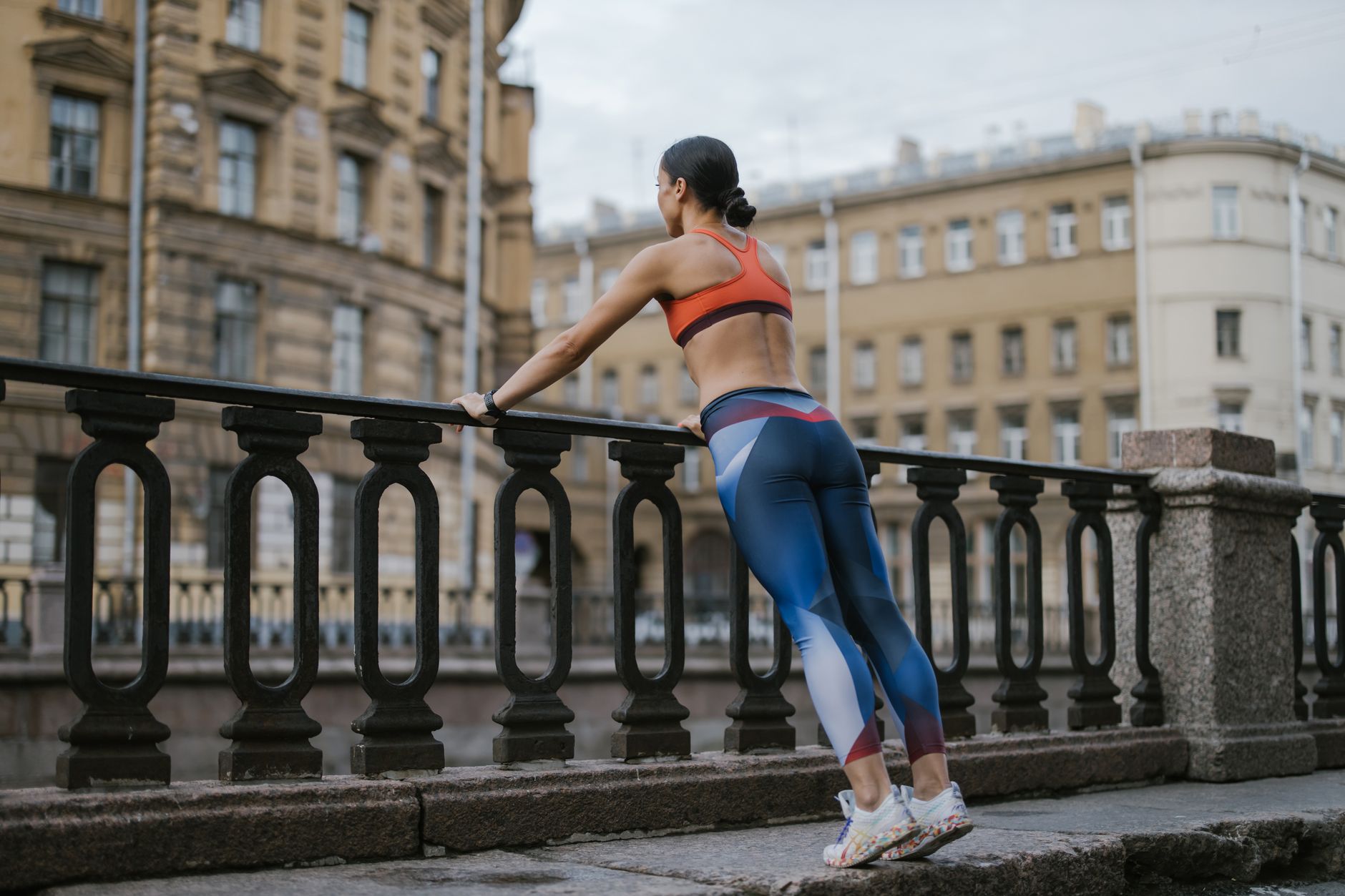 Female athlete in sportswear leaning against railing in a city environment.