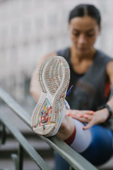 Close-up of a woman stretching on a rail in a city setting.