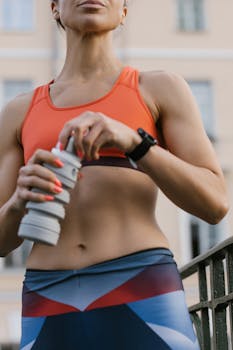 Fit woman in sportswear holding a water bottle during outdoor workout session.
