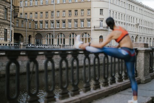 Woman stretching in sportswear on a riverside with urban architecture in the background.