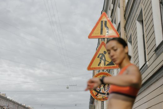 一个穿着运动服的女人身影模糊，在城市道路标志的背景下查看手表