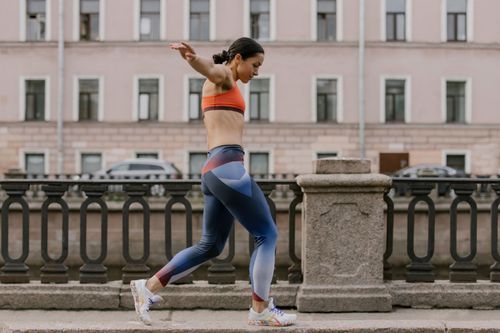 Free Woman in colorful activewear balancing on a sidewalk in front of a classic building. Stock Photo