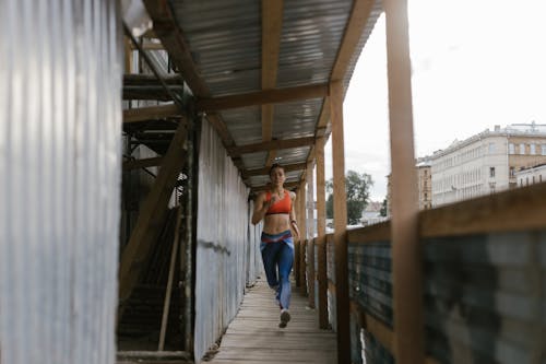 Free A Woman in Orange Sports Bra Running on the Passage Stock Photo