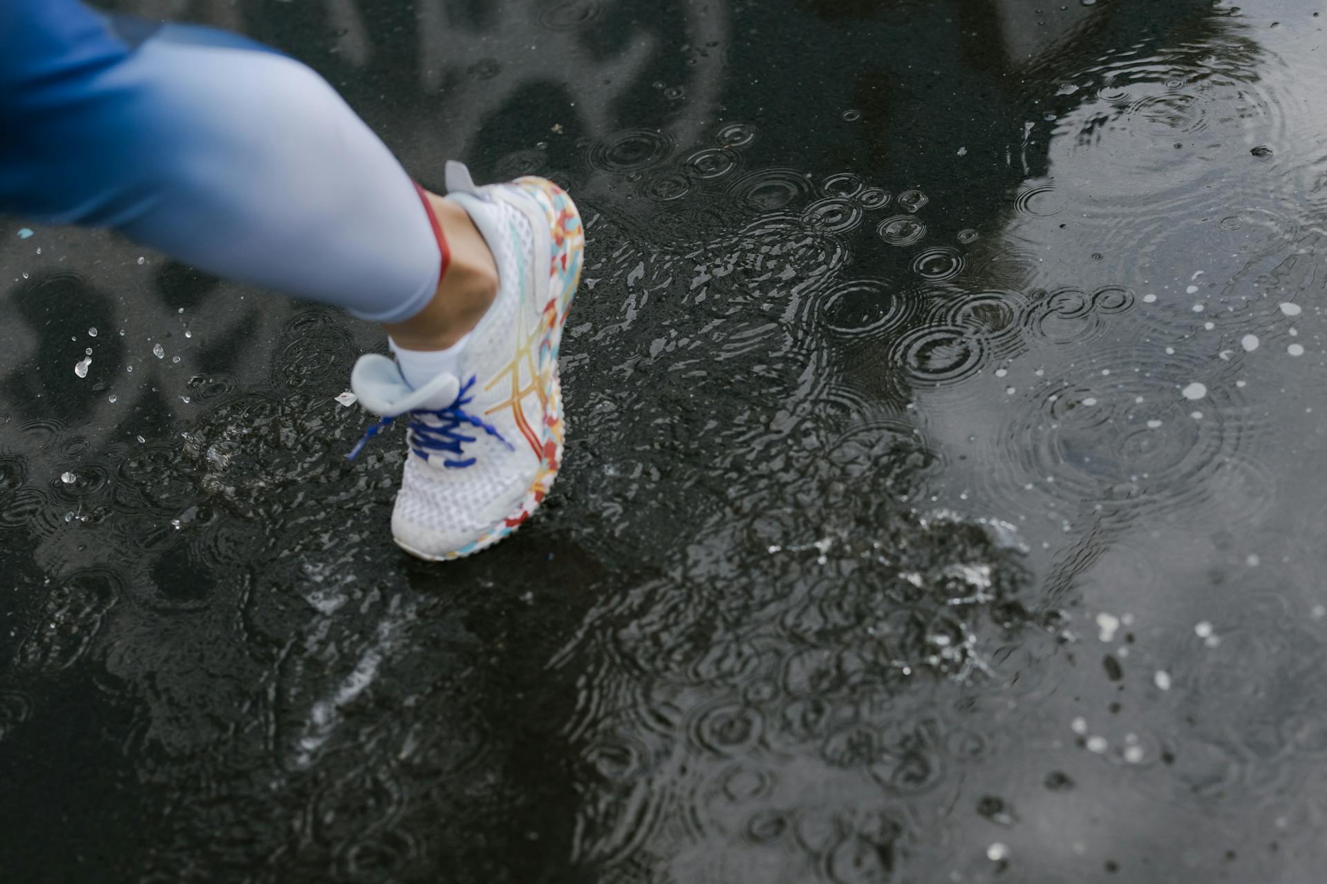 A Person Wearing a White Shoes while Stepping on Wet Road