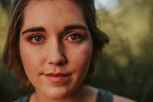 Closeup of positive female with short hair looking at camera while standing outside with green plants on blurred background in summer day - Fotografer Sidoarjo