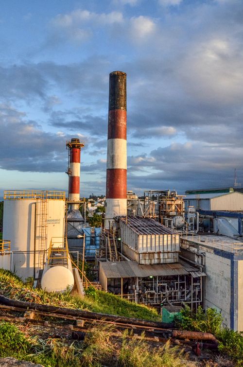Free A scenic view of a large industrial plant with tall smokestacks during sunset, surrounded by lush greenery. Stock Photo