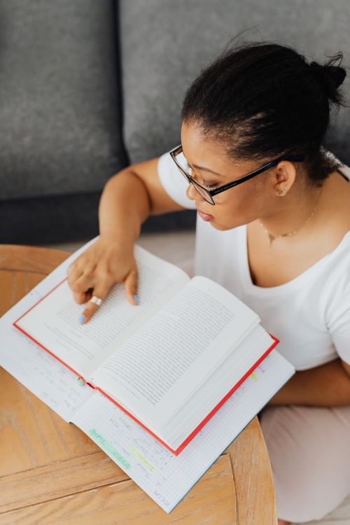 Free African American woman wearing glasses reading a book indoors, pointing at the text. Stock Photo