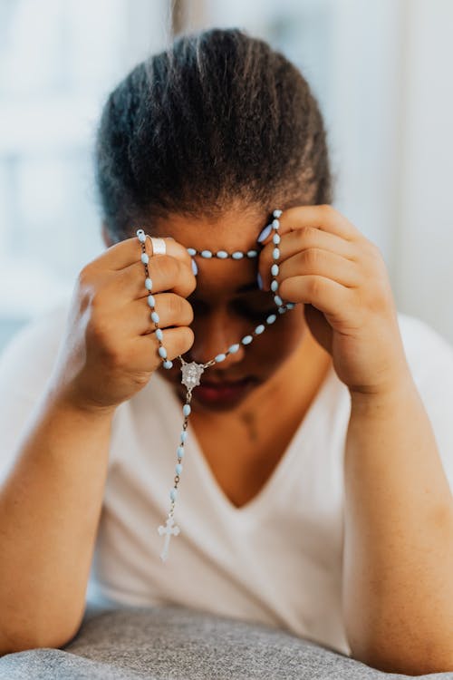 Free A Woman in White Shirt Praying while Holding a Rosary Stock Photo