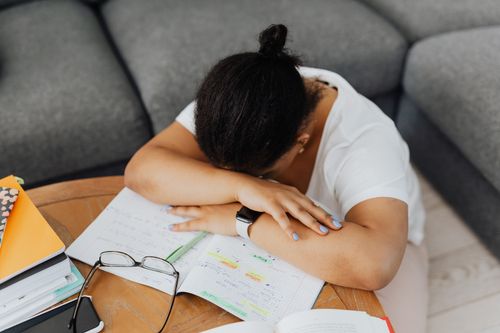 Free An exhausted student rests her head on a table surrounded by books, embodying study fatigue. Stock Photo