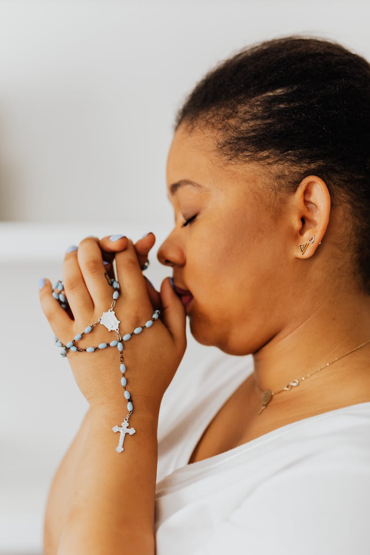 A Woman In White Shirt Praying While Holding A Rosary