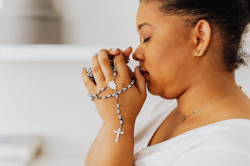 A Close-up Shot of a Woman Holding a Rosary while Praying