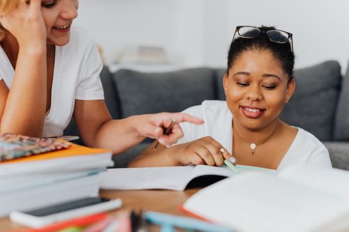 Free Two diverse women studying together with books in a cozy room setting. Stock Photo