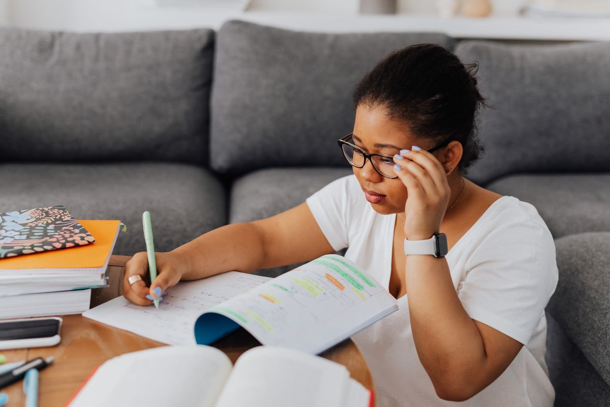 Mujer con gafas que estudia en el sofá de su casa y subraya sus apuntes