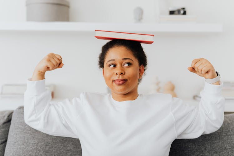 A Woman In White Sweater With A Book On Her Head