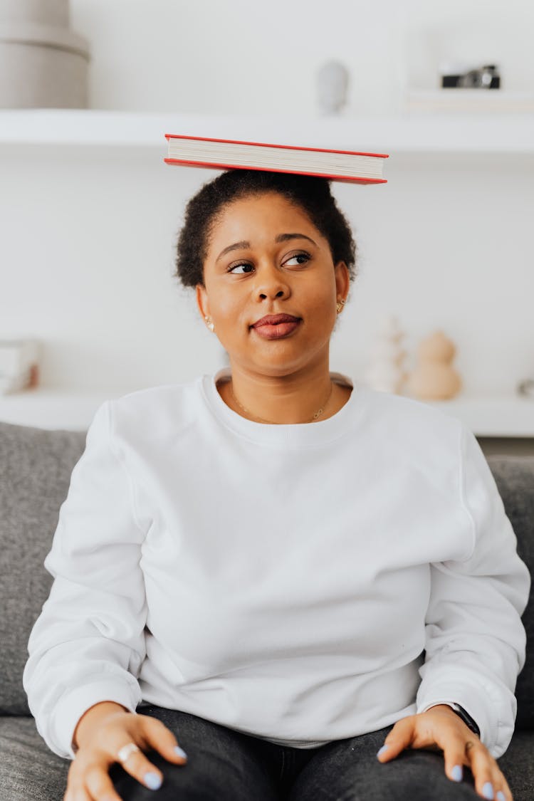 A Woman In White Sweater With A Book On Her Head