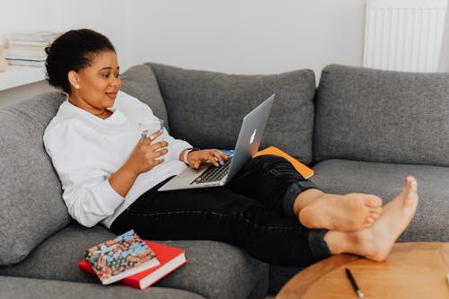 A Woman Casually Sitting on a Sofa while Using Her Laptop