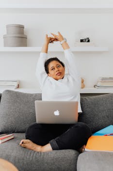 Woman stretching with a laptop on a couch, emphasizing remote work and relaxation.
