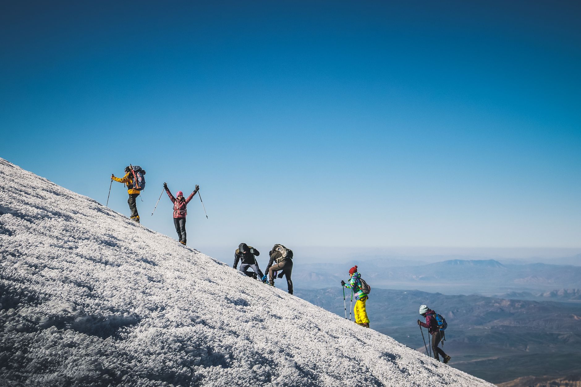 Adventurous group climbing a snowy mountain under clear blue skies, showcasing determination and teamwork.