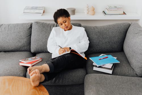 A Woman Casually Sitting on a Sofa while Doing Her Homework