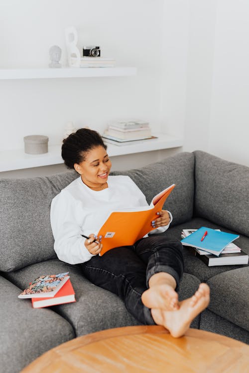 
A Woman Casually Sitting on a Sofa while Doing Her Homework