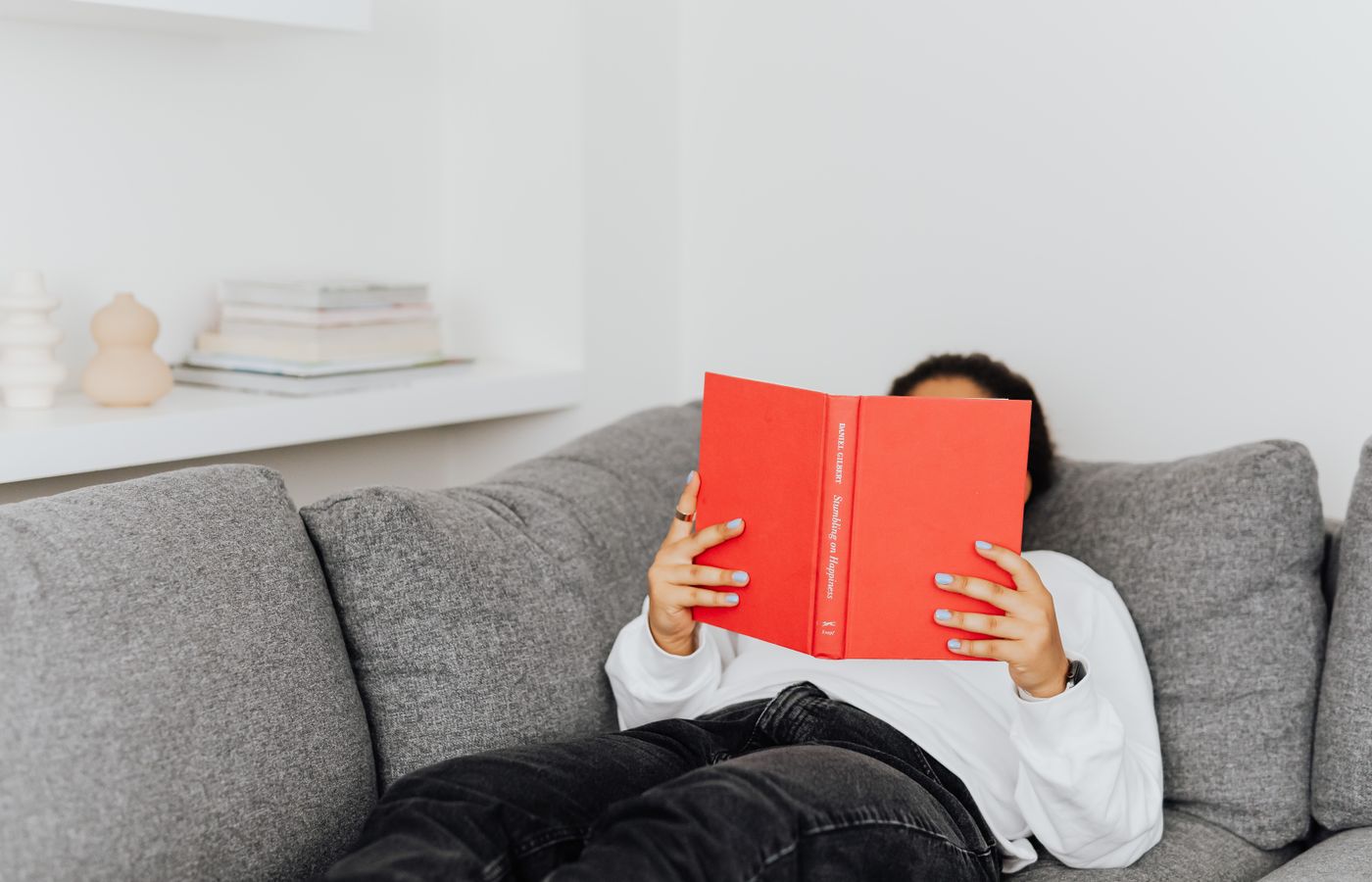 A relaxed person lying on a sofa reading a bright red book in a peaceful setting.