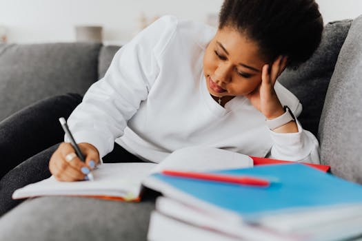 A young woman intensely focused on studying with notebooks and textbooks on a couch.